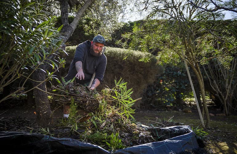 Un membre de l'équipe Parcs & Jardins ramasse les déchets verts sur une bâche pour nettoyer le terrain